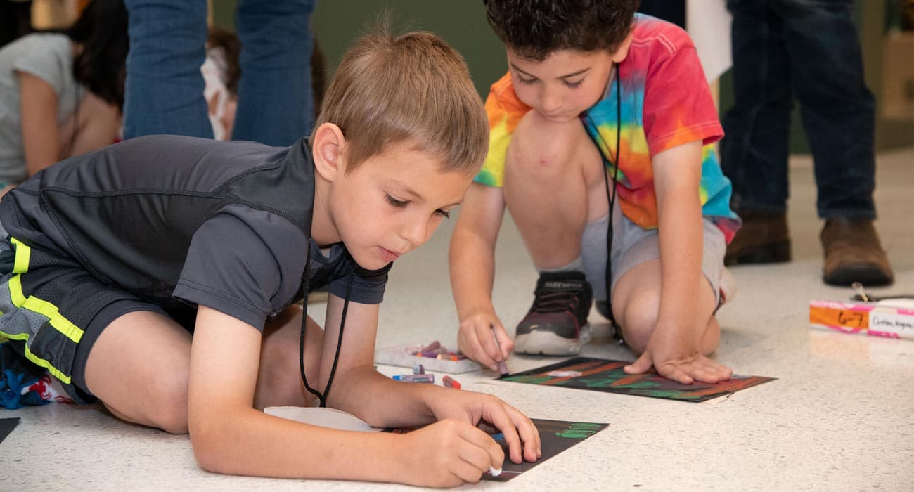 Two campers drawing on paper on the floor in the gallery.