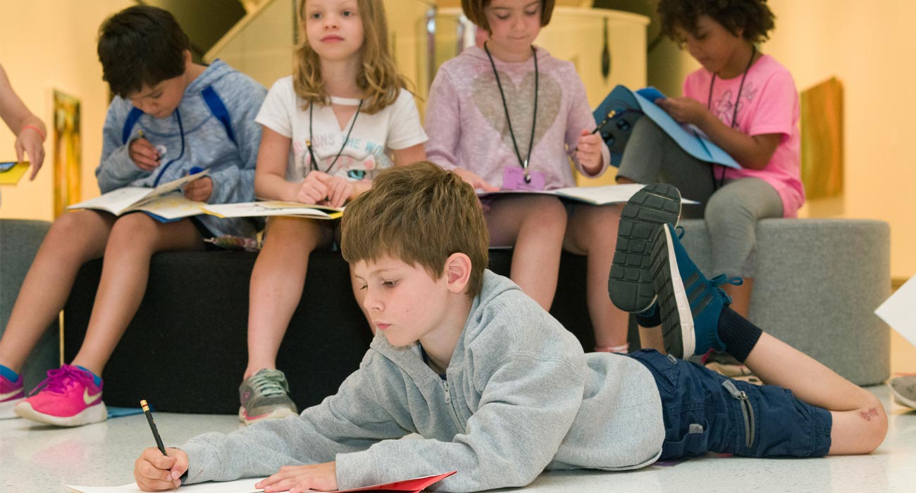 A boy draws with paper on the floor.